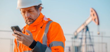 Petrol ve gaz işlemini denetlerken cep telefonu kullanan sondaj kulesi mühendisi, alandaki sondaj performansını izleme, seçici odaklanma