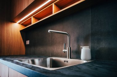 Su musluğu ve metalik lavabo modern parlak mutfakta kurşun şeritli ışık, seçici odak