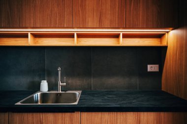 Su musluğu ve metalik lavabo modern parlak mutfakta kurşun şeritli ışık, seçici odak