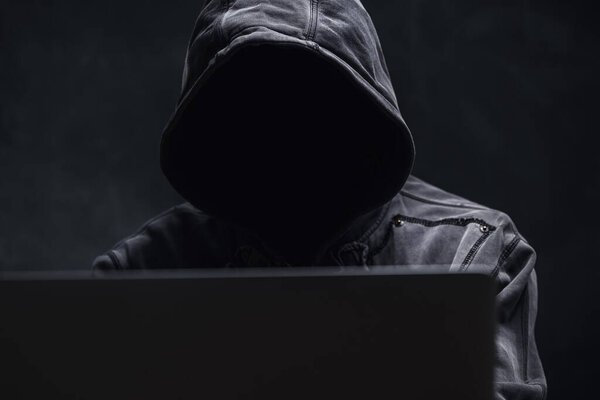 Hooded computer hacker using laptop computer, selective focus