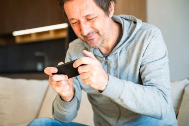 Evde cep telefonuyla video oyunu oynayan adam, seçici odaklanma