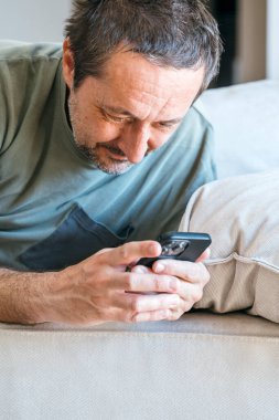 Oturma odasındaki kanepede uzanırken cep telefonu kullanan tembel patates adam.