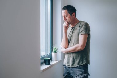 Ciddi bir beyaz erkek pencereden bakar ve düşünür, seçici bir odak