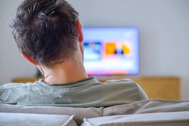 Kanepede oturan ve oturma odasında televizyon izleyen, seçici odaklı erkek görüntüsü.