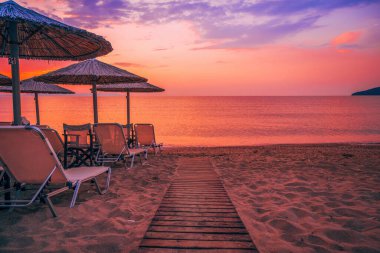 Yunanistan 'ın Vrasna plajında yaz gündoğumunda Palapa sazlık güneş şemsiyeleri. Seçici odak.