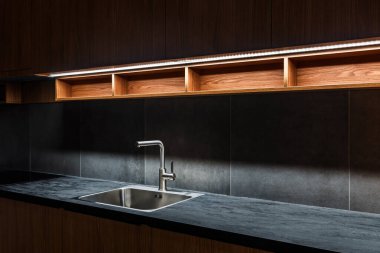 Su musluğu ve metalik lavabo modern parlak mutfakta kurşun şeritli ışık, seçici odak