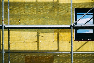 Mineral yünlü ev yalıtımı. İnşaat alanı iskelesi ve yüksek yoğunluklu yalıtım malzemesi yapı cephesinde. Seçici odak.