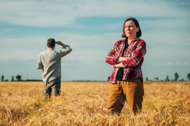 Olgun buğday tarlasında poz veren erkek ve dişi çiftçiler hasat için hazır, seçici bir odaklanma.