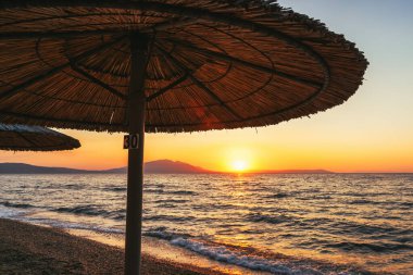 Yaz gündoğumunda Yunanistan 'ın Vrasna kentindeki plajda Reed şemsiyeleri. Seçici odak.