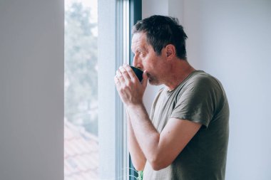 Düşünceli bir adam sabahleyin pencereden dışarı bakıp düşünürken kahve içiyor. Güne başlamak için kafein dozu. Seçici odak.
