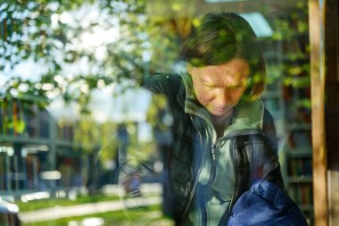 Genel kütüphane rafında kitaplara göz atan sıradan bir kadının portresi, geniş pencereden görülüyor, seçici odak noktası