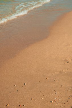 Deniz dalgalarının kumlu kıyı şeridine ve çakıl taşlarına vurduğu güzel deniz manzarası, seçici bir odak noktası.