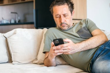 Oturma odasındaki kanepede uzanırken cep telefonu kullanan sıkıcı patates adam.