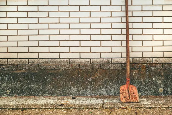 Kopya alanı olarak beyaz tuğla duvara yaslanmış eski paslanmış kürek.
