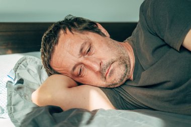 Morning depression and lethargy, portrait of mature adult male laying in bed, selective focus