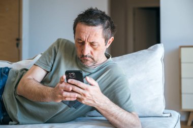 Oturma odasındaki kanepede uzanırken cep telefonu kullanan sıkıcı patates adam.