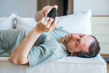 Oturma odasındaki kanepede uzanırken cep telefonu kullanan tembel patates adam.