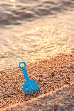 Mavi plastik kürek çakıllı kumsalda sıkışmış altın ışık yumuşak deniz dalgalarından yansıyor. Seçici odak.