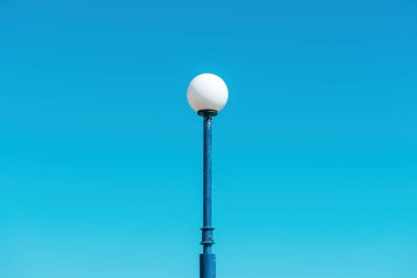 Yunanistan 'ın Halkidiki kentinde açık mavi gökyüzüne karşı yuvarlak beyaz küresi olan bir sokak lambasının minimalist görüntüsü. Seçici odak.