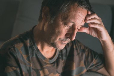 Stresli, eli alnında, evde oturan, anksiyete ya da tükenmişlikle uğraşan, seçici odaklı olgun bir adam.