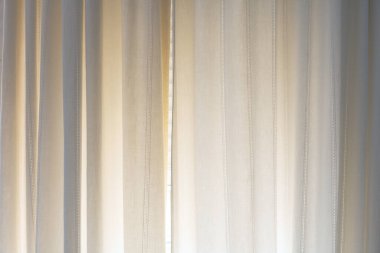 Dikey dikişli saf bej perdeler doğal gün ışığıyla hafifçe aydınlatılıyor. Sakinleştirici, sıcak tonlu minimal iç dekorasyon. Soyut arkaplan.