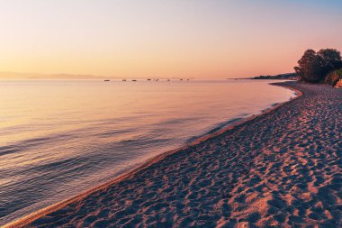 Yunanistan 'ın Halkidiki kentindeki Polychrono' da sakin Ege Denizi üzerinde huzurlu bir gün doğumu. Altın ışık kumlu sahilde uzun gölgeler oluştururken balıkçı tekneleri ufukta süzülüyor. Seçici odak.