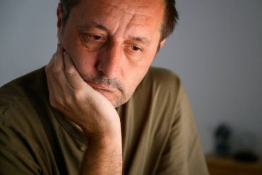 Kapalı mekanda somurtan bir adamın sade portresi karamsar ve dramatik ışıklandırma hüznü, yalnızlığı ve içgözlem yapmayı vurguluyor. Seçici odak.