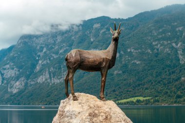 Bohinj, Slovenia - August 24, 2025: Statue of gold horned chamois Goldhorn (Zlatorog) on the rock with lake Bohinj in background