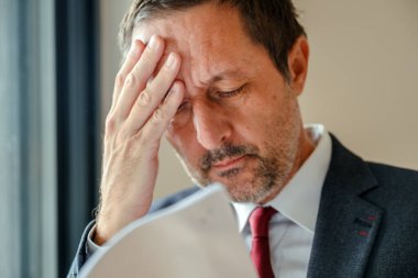 Concerned manager with headache reviewing stressful finance report at workplace. Selective focus.
