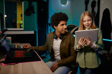 Mobil dijital tablet kullanarak müzik stüdyosunda çalışan genç kız şarkıcıyla ses mühendisi