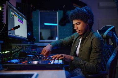 Mutlu gülümseyen radyo sunucusunun portresi stüdyodaki masada ses mikseri kullanıyor, DJ kulaklık takıyor radyo istasyonunda çalışıyor.