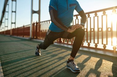 Yetişkin fitness koşucusu, şehir köprüsünde koşmadan önce bacaklarını esnetiyor. Yakın görünüm