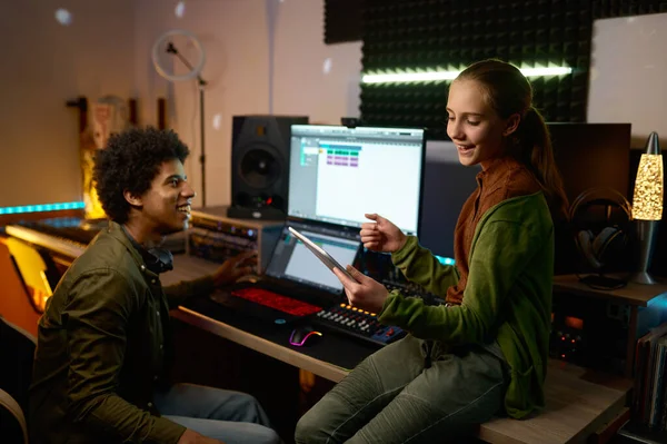 Audio engineer with young girl singer working in music recording studio using mobile tablet