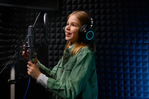 年轻的少女歌手头戴耳机 带着麦克风在录音棚演唱新歌 — 图库照片