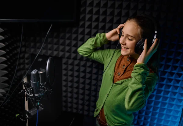 年轻的少女歌手戴着耳机在录音室用麦克风唱新歌 — 图库照片