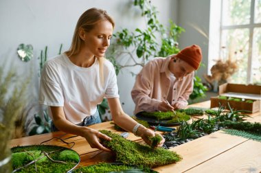 Yaratıcı sanat stüdyosunda çalışan profesyonel çiçekçiler. Yeşil taze yosunlardan kompozisyon yapan genç kadına odaklan.