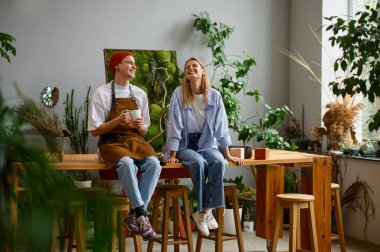 Çiçek atölyesi. Profesyonel bir çiçekçi masada oturmuş gülümsüyor ve konuşuyor.
