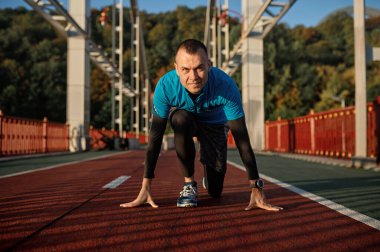 Başlangıç konumundaki yetişkin hız koşucusunun portresi spor pistinde koşmaya hazır