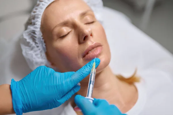 女性のクライアントの顔に滅菌手袋で美容師の手 現代の美容クリニックでのアンチエイジング注射や整形手術 クローズアップビュー — ストック写真