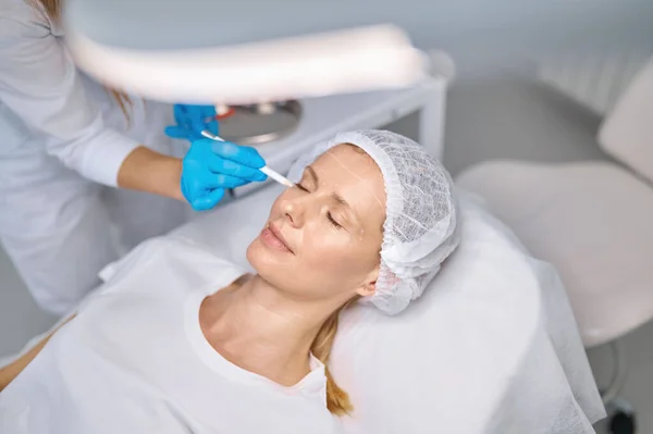 Kosmetologe Mit Weißen Bleistiftzeichnungen Kundengesicht Bereitet Frau Auf Verjüngungskur Vor — Stockfoto