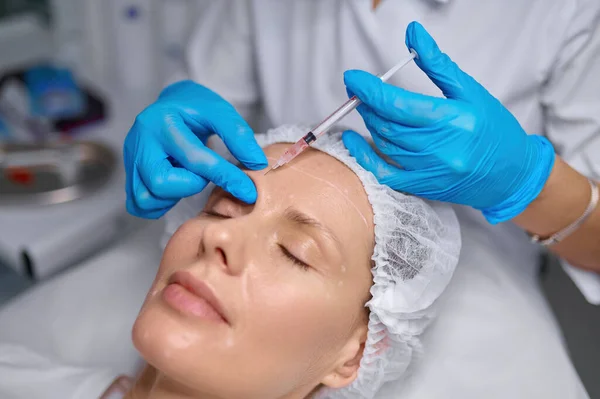 アンチエイジング治療と眉への充填剤注射 サイドビュー美容師は 患者の皮膚の穿刺を入れて — ストック写真