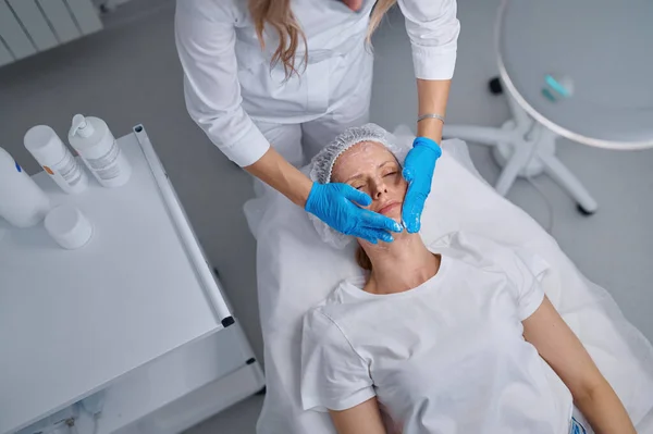 女性プロの医師美容師は スキンケアのために患者の顔にマスクを適用します スキンケア 若返りと栄養のための化粧品手順 — ストック写真