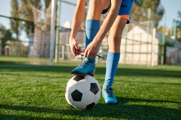 小个子足球运动员把鞋带系在鞋带上 把腿放在足球上 在体育学校准备训练比赛 — 图库照片