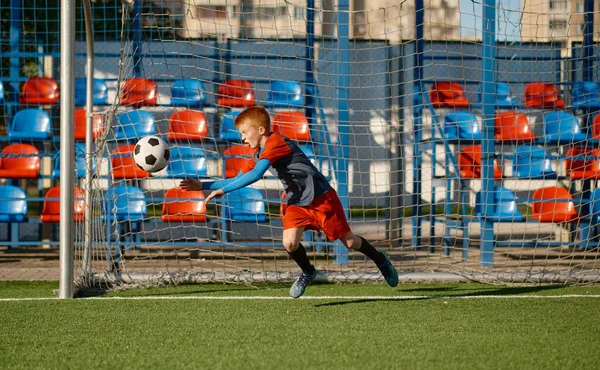 Junior goalkeeper catching ball while defending gate in football match. Soccer team practice or competition tournament