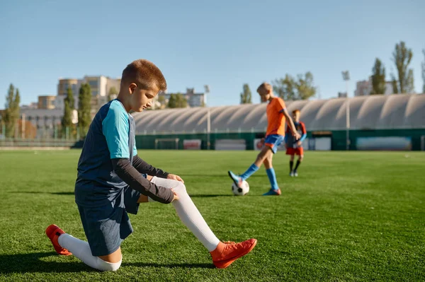 活跃的孩子们在室外绿色运动场上踢足球 把重点放在男孩调整袜子的前景 — 图库照片