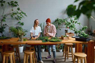 İki mutlu ve gülümseyen çiçekçi yaratıcı atölyede birlikte çalışıyor. Genç adam ve kadın iç tasarım için güzel ev dekorasyonu yapıyorlar.
