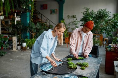 Genç bir çift çiçek tasarımcısı yosun ve eğrelti otu yapraklarıyla taze kesilmiş yeşil tabaklar hazırlıyor. Sanat atölyesi tasarımı iç tasarım