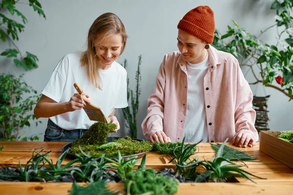 Young florists working at creative workshop. Millennial hipster man and woman making decoration from fresh herbs