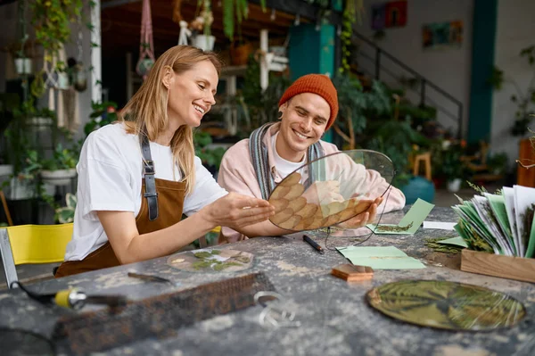 Sanat atölyesinde çalışan genç dekoratörler. Yetenekli hipster erkek ve kadın masada oturuyor ve doğal tasarım elementinden soyut modern sanat yaratıyorlar.