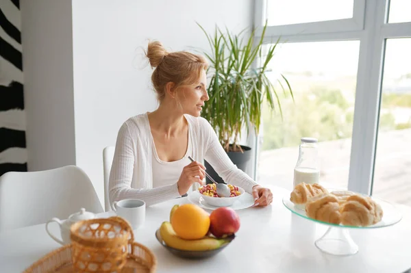 若い女性は家庭のキッチンで健康的な朝食を楽しんでいます 魅力的なスリム女の子食べるボウルのシリアル自家製デトックス食品 — ストック写真